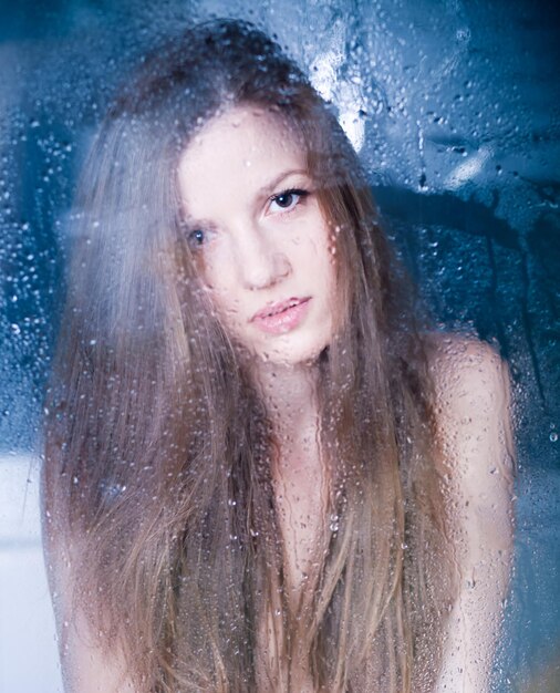 Cute woman behind window with rain drops on window