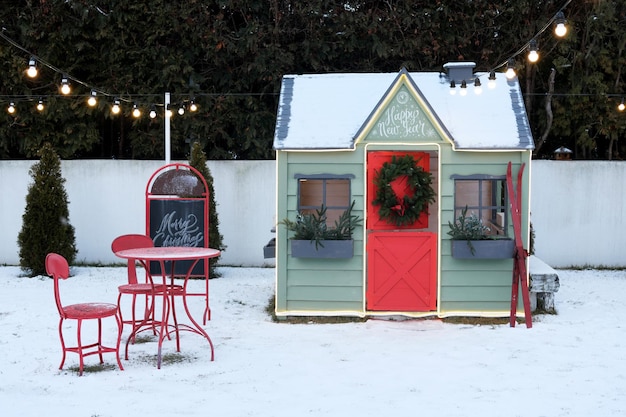 Cute wooden painted redgreen private children play house in home garden decorated with Christmas wreath outdoors in cold snowy winder evening