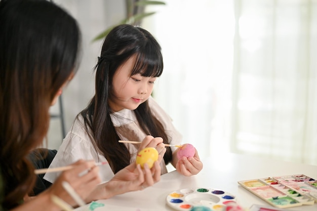 A cute young Asian girl focuses on painting Easter eggs with watercolors Happy family and holiday