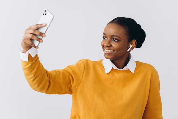 Cute young black lady with stylish dreadlocks taking selfie on smartphone for social media or friends, positive african american woman having fun at home, using mobile phone, copy space