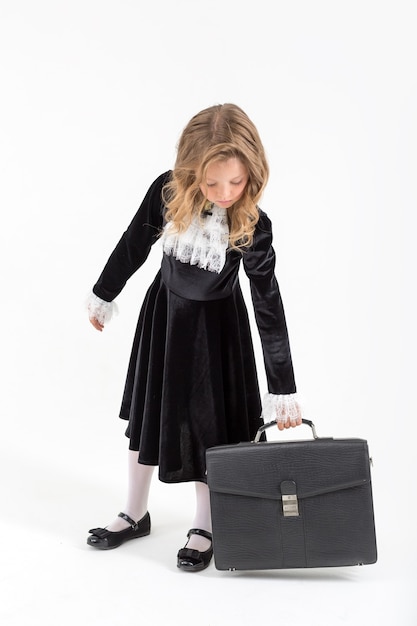 Cute young blonde schoolgirl in a school black dress on an isolated white