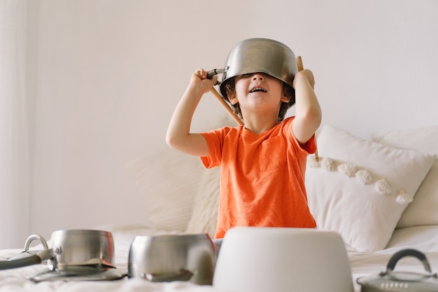 Cute young boy using wooden sticks to bang saucepans that are set up like a drumset. 