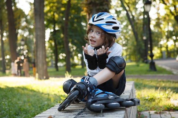 Cute young boy wearing helmet and skates, resting after rollerblading at the park