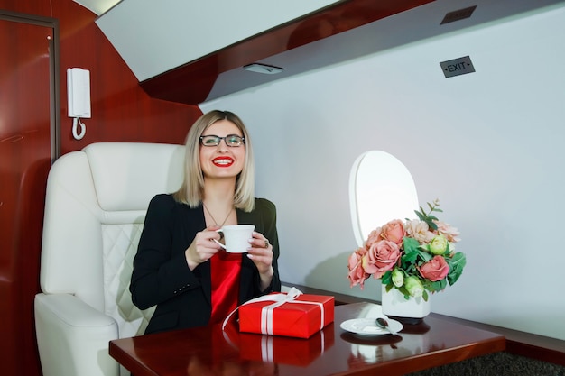 Cute young businesswoman with gift flying in luxury private jet