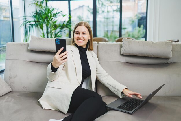 Cute young freelancer woman in casual clothes relaxing on sofa while working on internet via netbook while remote working on project at home