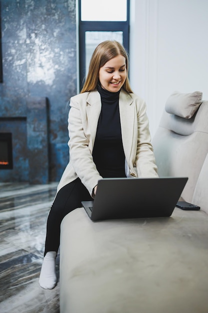 Cute young freelancer woman in casual clothes relaxing on sofa while working on internet via netbook while remote working on project at home