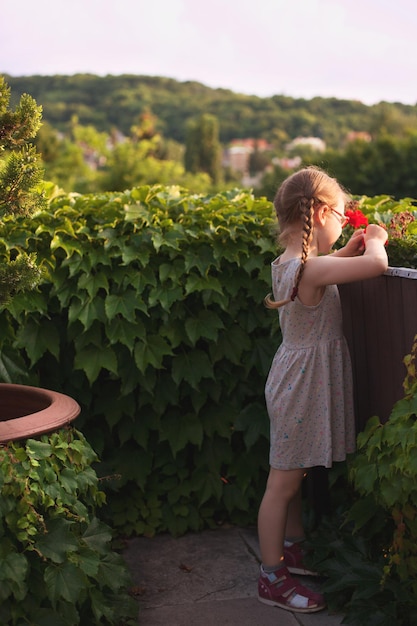 Cute young girl in a beautiful dress playing with flowers on the balcony