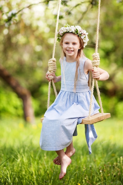 Cute young girl  having fun on a swing in blossoming old apple tree garden. Sunny day. Spring outdoor activities for kids