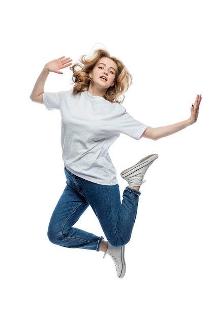 A cute young girl is jumping A teenager in a white Tshirt and blue jeans Activity and positive Isolated on white background Vertical