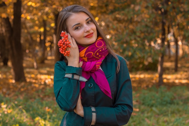 Cute young girl in Scharfe stands in the Park and holds in her hand a sprig of Rowan closeup