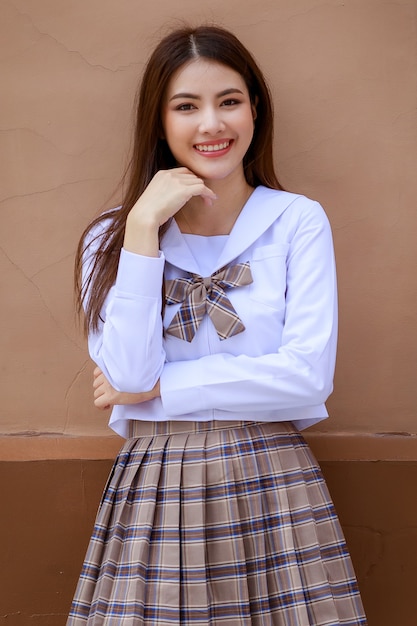 Cute and young girl wearing Japanese, Korean style schoolgirl uniform and pose to camera with fun and happy in front of school building.