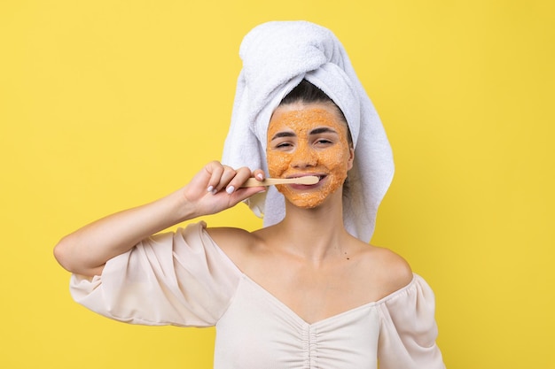 A cute young girl with a scrub mask on her face brushes her teeth against a yellow background