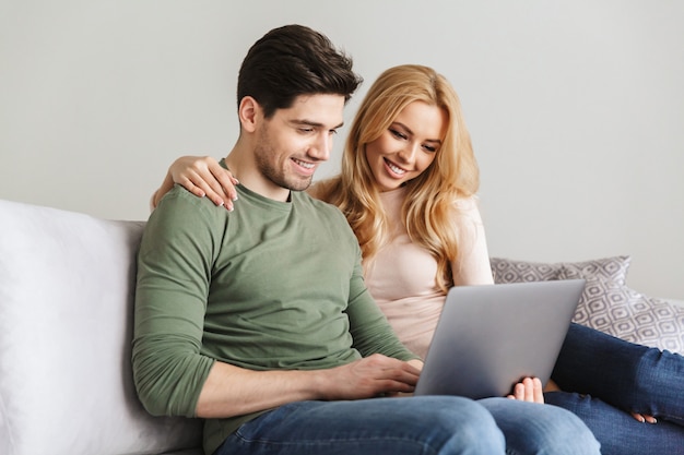 Cute young loving couple sitting on sofa using laptop computer.