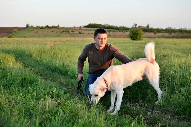 Cute young man walking with him dog outdoors in green grass summer