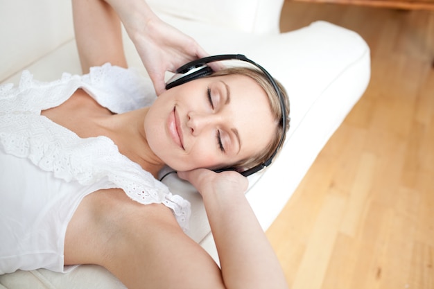 Cute young woman listening music lying on a sofa 