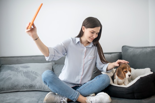 A cute young woman making selfie with her puppy and looking happy