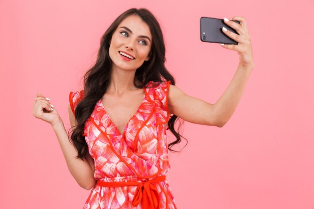 Cute young woman posing isolated wall take a selfie by mobile phone.