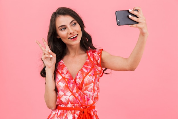 Cute young woman posing isolated wall take a selfie by mobile phone.