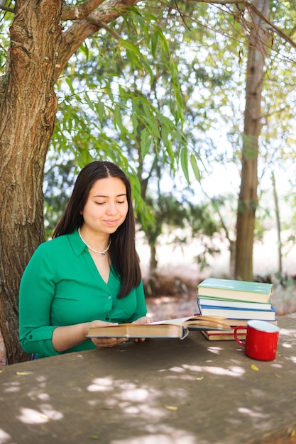 Cute young woman reading books in the field under a willow tree with a coffee mug World book day