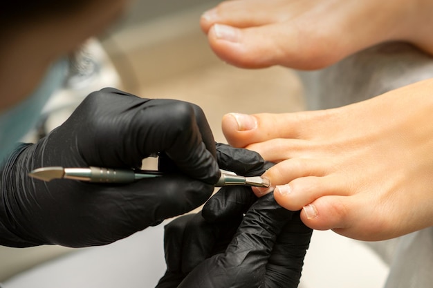 Cuticle Removal on Toes. Hands in black gloves of pedicure master remove cuticle on female toes by pusher.