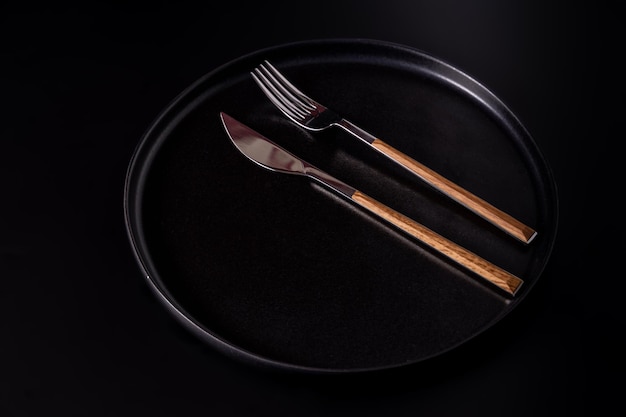 Cutlery on a black plate isolated on a black background top viewflat lay