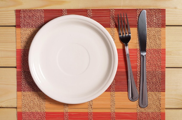 Cutlery and empty plate on bamboo napkin top view