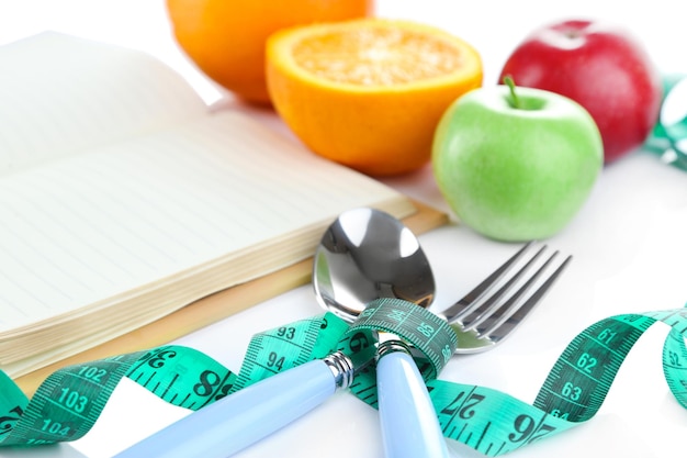 Cutlery tied with measuring tape and book with fruit close up