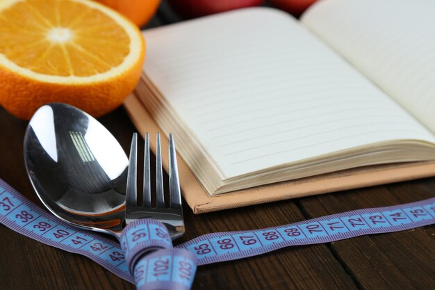 Cutlery tied with measuring tape and book with fruits on wooden background