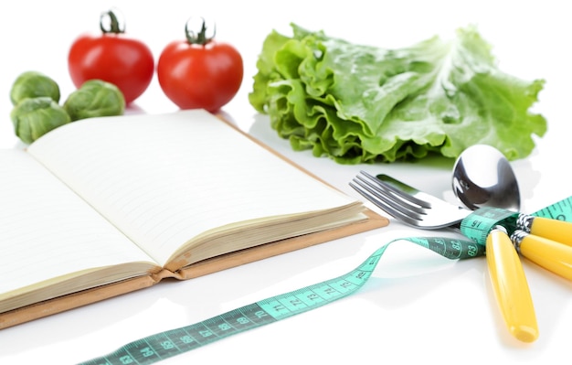 Cutlery tied with measuring tape and book with vegetables isolated on white