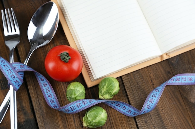 Cutlery tied with measuring tape and book with vegetables on wooden table