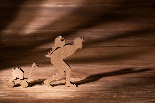 Cutout cardboard man carrying keys to his new house on his back Wooden background Rising mortgages