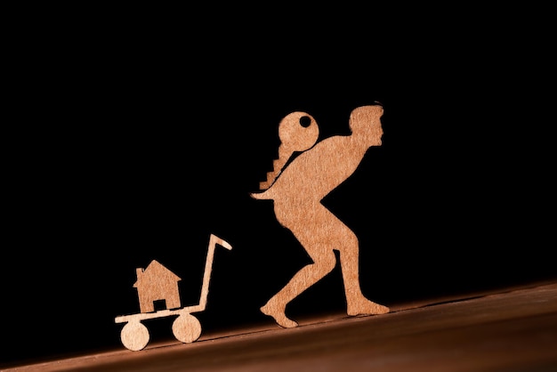 Cutout cardboard man carrying uphill the keys to his new house on his back Rising mortgages