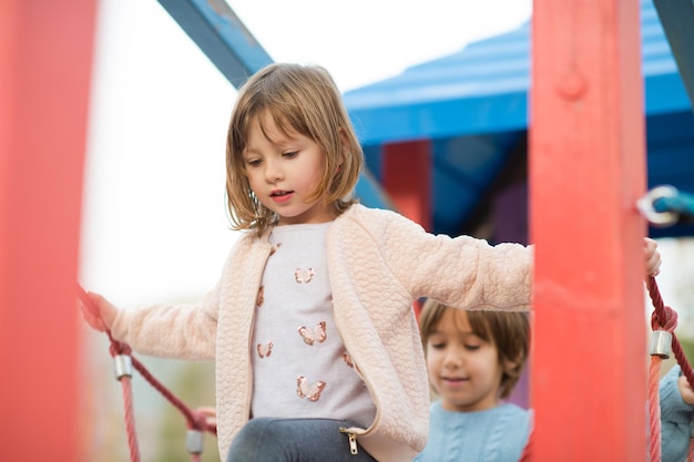 cutte little girl and boy in childrens park having fun and joy while playing in playground on autumn cloudy day