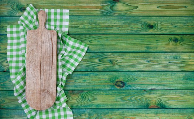 Cutting board on green checkered tablecloth, top view