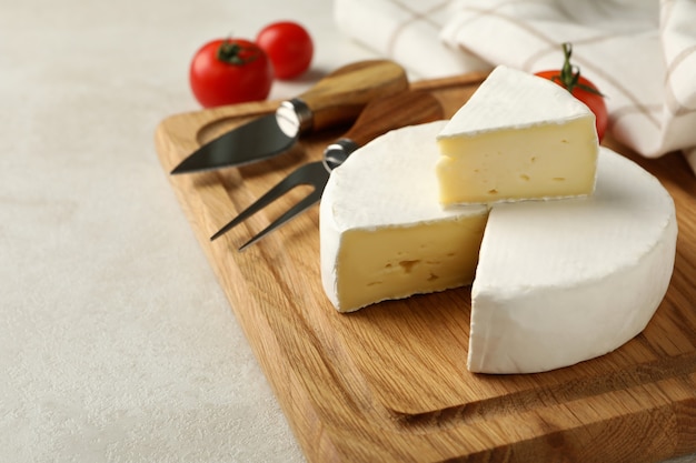 Cutting board with camembert cheese, tomato, fork and towel on white textured background