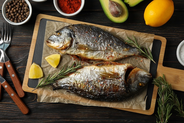 Cutting board with fried Dorado fishes and spice ingredients on wooden