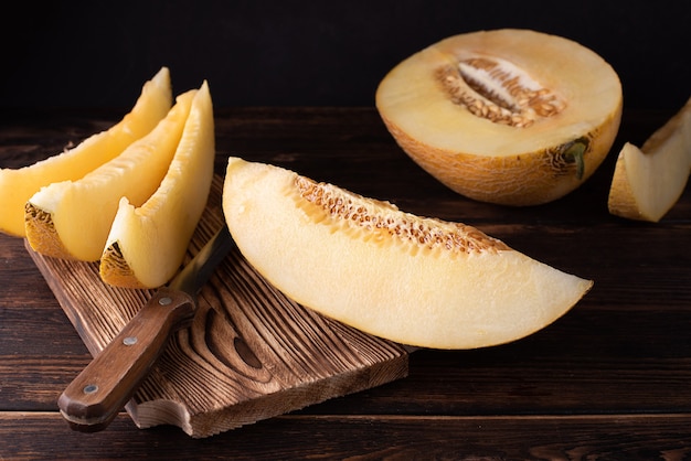 Cutting board with juicy melon slices and half on dark wooden background, healthy food.