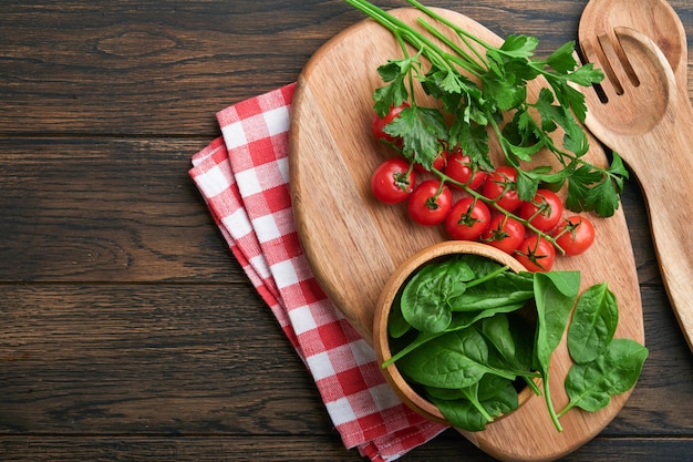 Cutting board with kitchen spoons and red napkin and parsley tomato for cooking on old wooden dark background Vegetarian food health or cooking concept Food background with free space for text