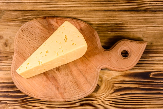 Cutting board with piece of cheese on wooden table Top view