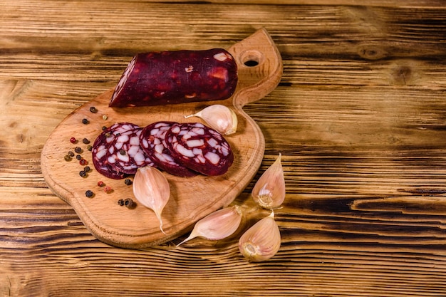 Cutting board with sliced salami sausage and garlic on rustic wooden table