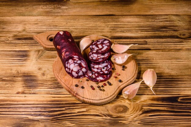 Cutting board with sliced salami sausage and garlic on rustic wooden table