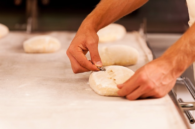 Cutting the dough. Close-up of male hands cutting the dough with special knife