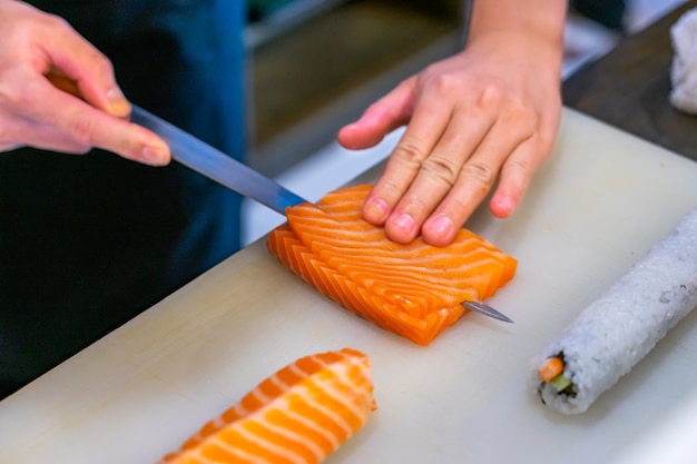 Cutting the salmon with a knife, Japanese chef making sashimi in kitchen, Sushi are made