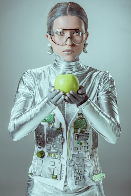 cyborg in futuristic eyeglasses holding apple and looking at camera isolated on grey future