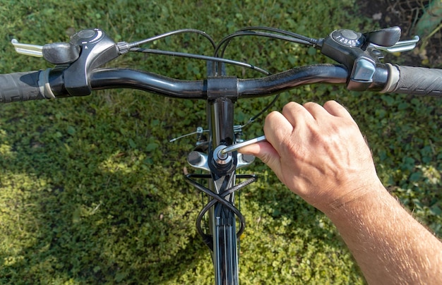 A cyclist adjusts the handlebars of a bicycle with a tool on street while walking Urgent bike repair