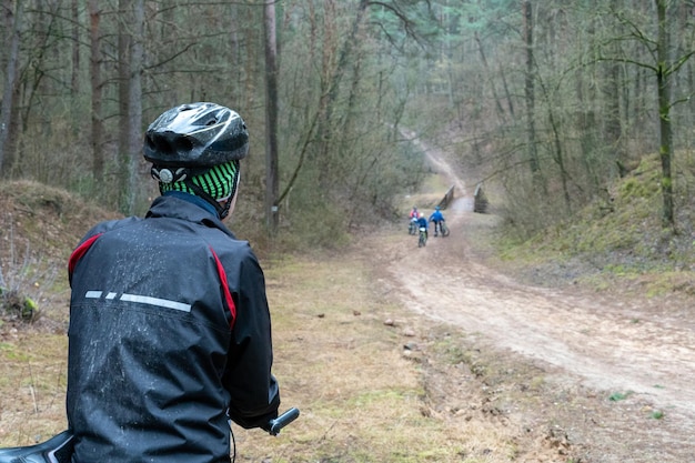 Cyclist in dirty clothes watching cycling race in the forest The jacket is black Sandy trail descends from the mountain across the river Spending time in nature Do sports in bad weather Fresh air