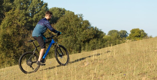 Cyclist in pants and fleece jacket on a modern carbon hardtail bike with an air suspension fork rides offroad The guy is resting on a bench in the autumn park