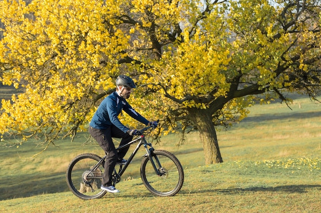 Cyclist in pants and fleece jacket on a modern carbon hardtail bike with an air suspension fork rides offroad The guy is resting on a bench in the autumn park