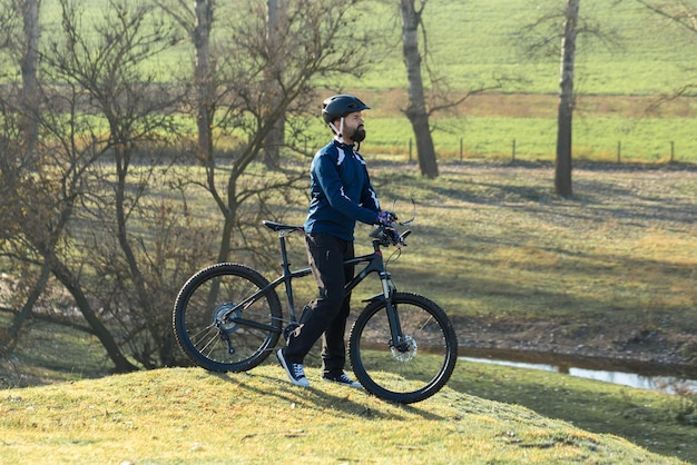 Cyclist in pants and fleece jacket on a modern carbon hardtail bike with an air suspension fork rides offroad The guy is resting on a bench in the autumn park