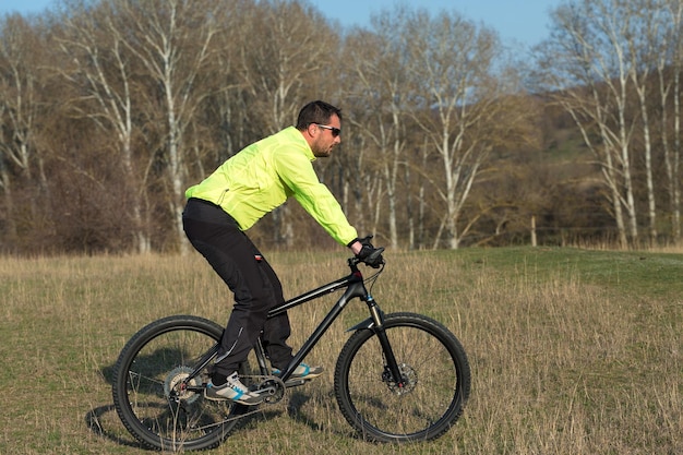 Cyclist in pants and green jacket on a modern carbon hardtail bike with an air suspension fork The guy on the top of the hill rides a bike